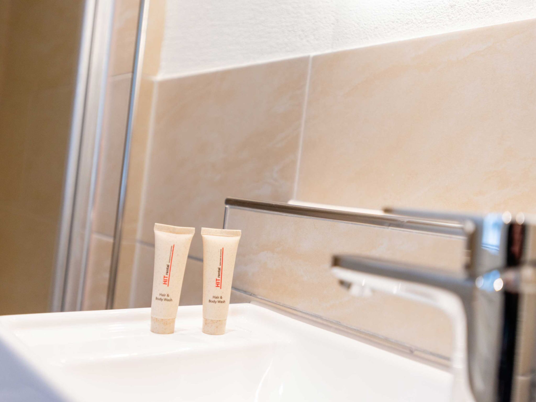 Deux tubes de shampoing et de gel douche pour cheveux et corps de la marque HIT sont posés sur le lavabo d’une salle de bain.