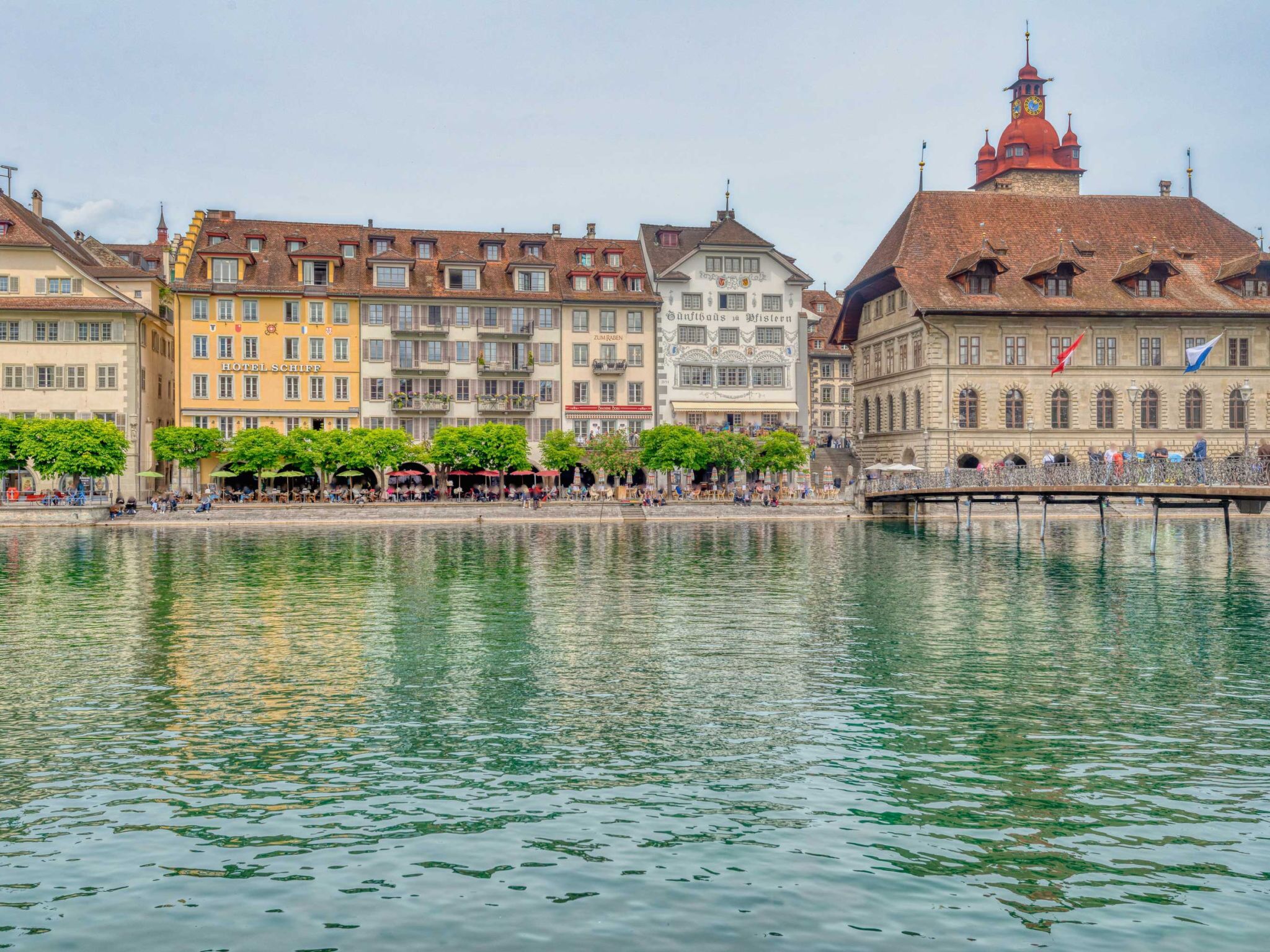Vista del río de un pueblo histórico europeo, con edificios a lo largo del agua, incluyendo un hotel con terraza.