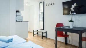 Ett modernt hotellrum med en säng, ett skrivbord, en stol, en krukväxt, en spegel och en väggmonterad lampa.