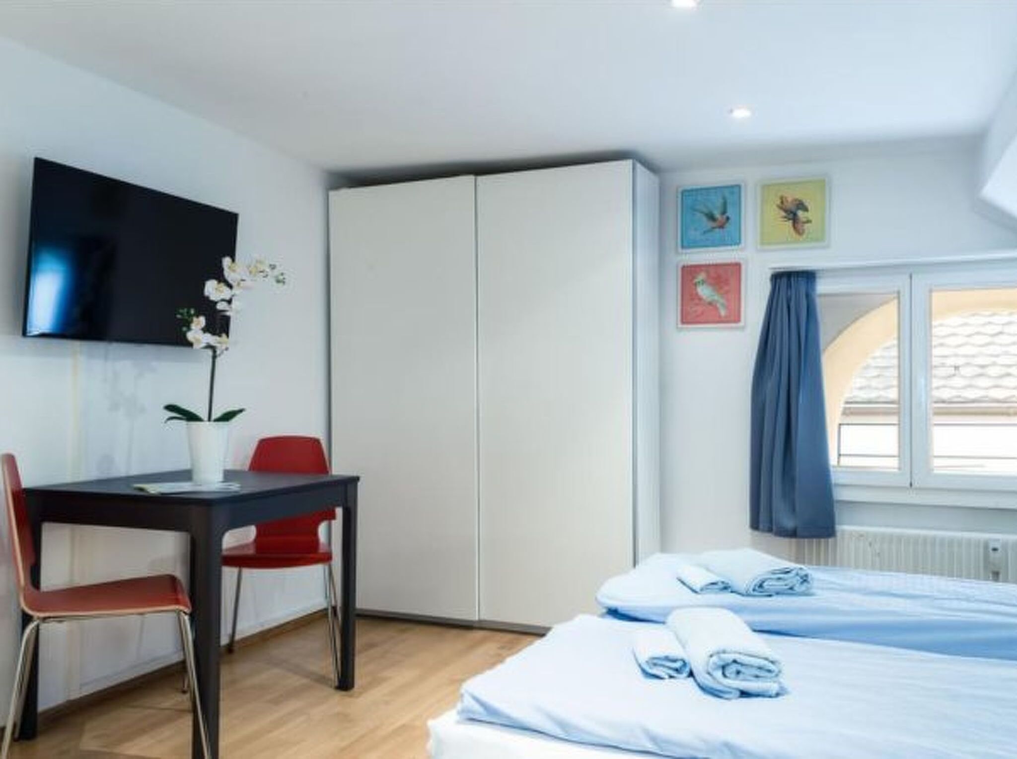 Quarto de hotel com cama, escrivaninha, cadeira, televisão e janela com cortinas.