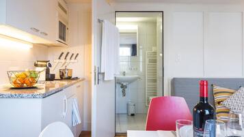 Een moderne keuken met witte kastjes, een aanrecht met fruitschaal, en een eethoek met een rode stoel en een tafel gedekt voor twee personen.