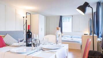 Een moderne, goed verlichte kamer met een eettafel gedekt voor twee personen, een bed met hoofdeinde en een groot raam met gordijnen.