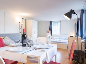 A modern, well-lit room with a dining table set for two, a bed with a headboard, and a large window with curtains. - Apartment  by Interhome (Zoug)