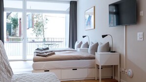 A modern bedroom with a large bed, bedside tables, a flat-screen TV, and a view of the outside. - Apartment  by Interhome (Basel)