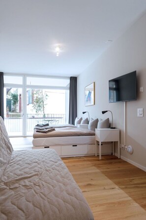 Ein modernes Schlafzimmer mit einem großen Bett, Nachttischen, einem Flachbildfernseher und Blick ins Freie.