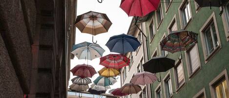 Une rue bordée de bâtiments des deux côtés, avec de nombreux parasols colorés suspendus au-dessus, et des gens qui se promènent.