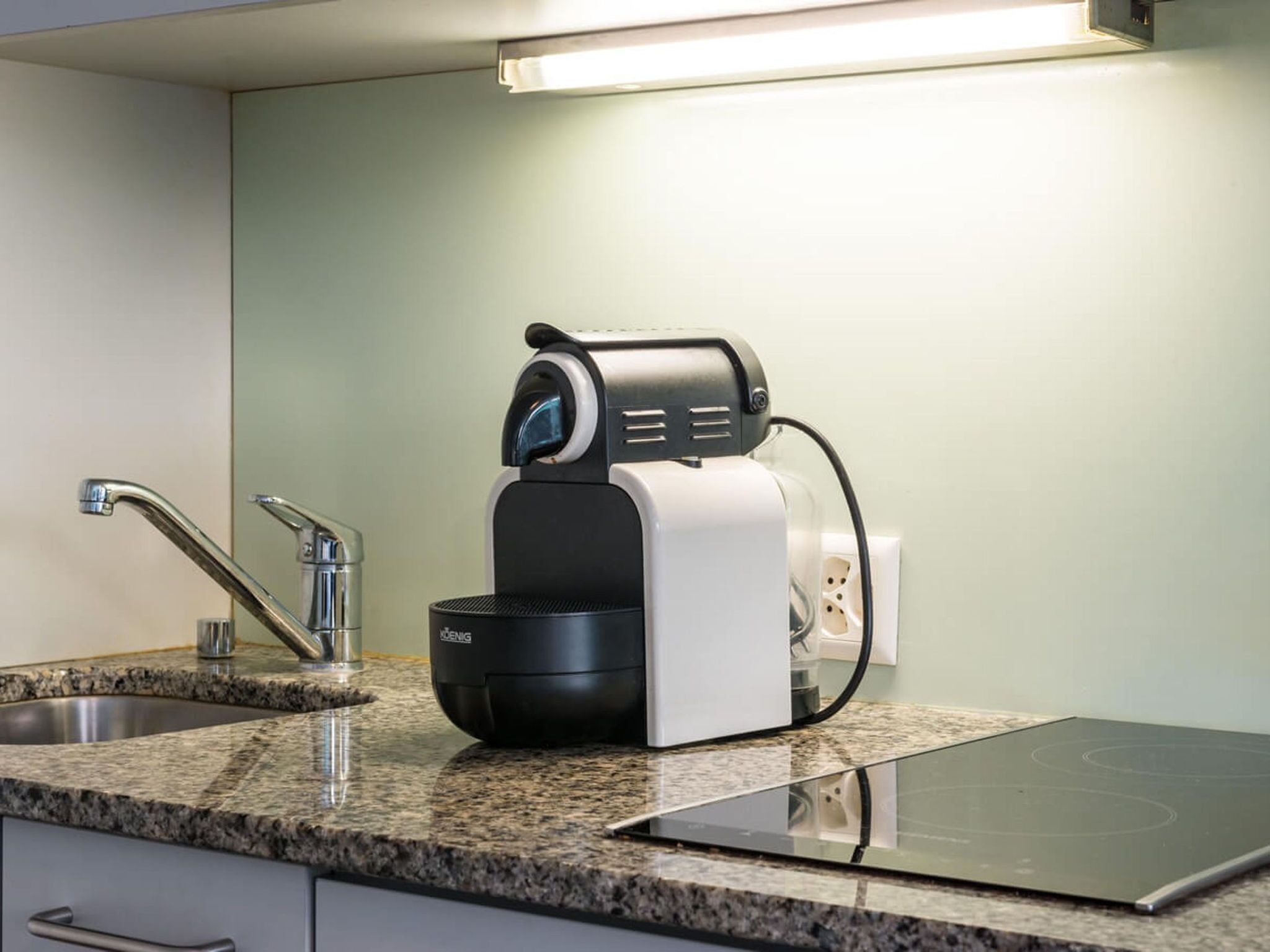 Eine Küche mit integriertem Induktionskochfeld, einer Kaffeemaschine und einem Spülbecken aus Edelstahl.