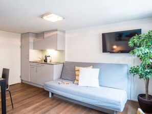 Ein gemütlicher Wohnbereich mit Küchenzeile, einer Couch, einem Fernseher und einem Blumentopf.