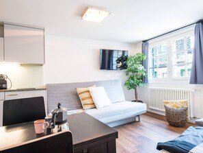 Ein modernes Hotelzimmer mit einer Couch, einem Esstisch, einem Wasserkocher und einem Fernseher.
