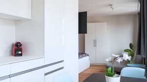 Ein modernes, minimalistisches Zimmer mit einem Bett, einem Esstisch und einem an der Wand befestigten Fernseher.