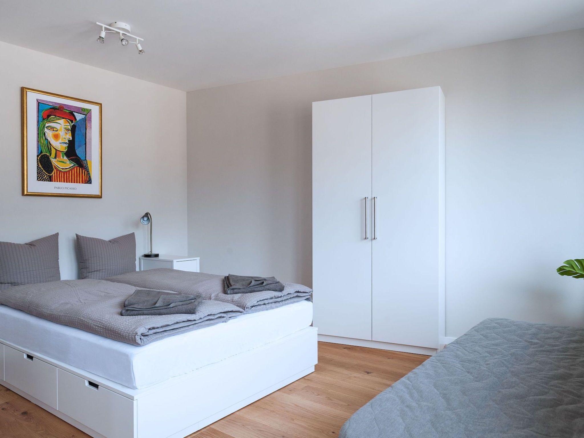 Ein modernes Schlafzimmer mit Bett, Kleiderschrank, Nachttisch und einem Gemälde an der Wand.