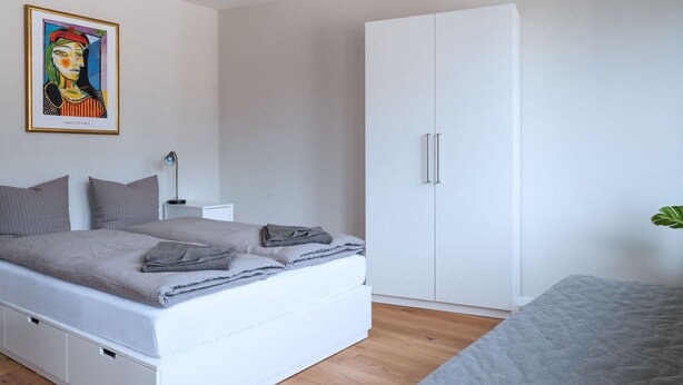 A modern bedroom with a bed, a wardrobe, a nightstand, and a painting on the wall. - Apartment  by Interhome (Basel)