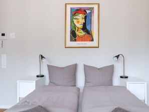 Ein Schlafzimmer mit zwei Betten, Nachttischlampen, einem gerahmten Kunstwerk an der Wand und einem weißen Nachttisch.