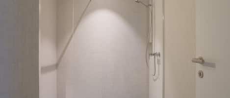 Un petit espace de douche fermé, doté d’un sol et de murs carrelés, d’un pommeau de douche et d’une porte avec une poignée.