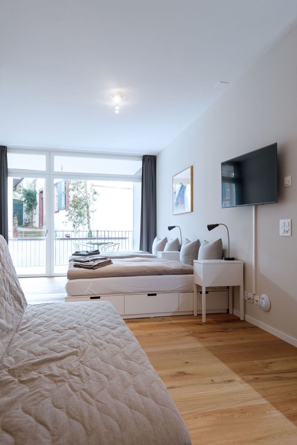 Ein modernes Schlafzimmer mit einem großen Bett, Nachttischen, einem Flachbildfernseher und Blick ins Freie.