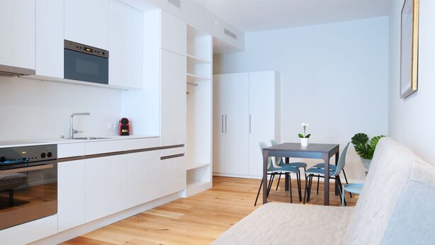 Une cuisine moderne avec des meubles blancs, un four encastré et un coin repas comprenant une table et des chaises.