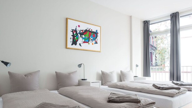 Une chambre d’hôtel moderne avec deux lits, une grande fenêtre avec des rideaux, un tableau au mur et une vue sur l’extérieur.