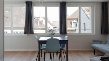 A room with a dining table, chairs, a sofa, and a window with curtains.