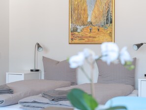 A bedroom with a bed, two bedside lamps, a painting on the wall, and a potted orchid. - Apartment  by Interhome (Basel)
