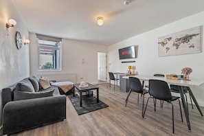Ein modernes Wohnzimmer mit Sofa, Couchtisch und Essbereich mit Stühlen sowie einem Fernseher.