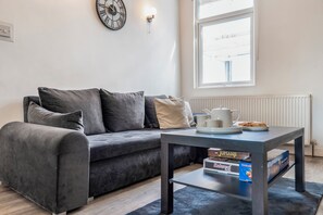 Ein modernes Wohnzimmer mit einem grauen Sofa, einem Couchtisch, einer Uhr und einem Fenster mit Blick.