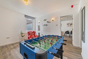 Ein Zimmer mit einem Kicker, einem roten Sofa, einem Fenster und einer Tür zu einem anderen Raum.