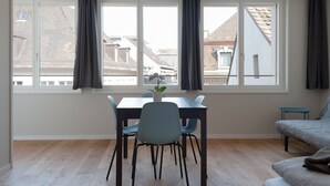 Een kamer met een eettafel, stoelen, een bank en een raam met gordijnen.