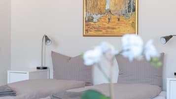A bedroom with a bed, two bedside lamps, a painting on the wall, and a potted orchid.