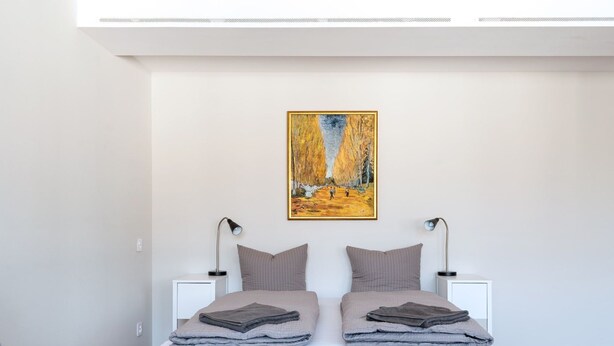 Een moderne slaapkamer met een wit bed, twee bedlampen en een schilderij aan de muur.