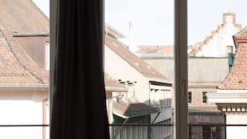 A window with a view of a building's roof and adjacent structures.