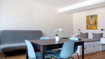 A modern living room with a sofa, a dining table with chairs, a potted plant, and a painting on the wall.