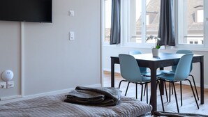 Een moderne kamer met een flatscreen televisie aan de muur, een eettafel met stoelen, en een raam met gordijnen.