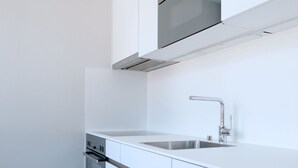 A modern kitchen with white cabinetry, a stainless steel sink, and a built-in oven. - Apartment  by Interhome (Basel)