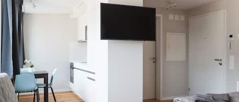 A modern hotel room with a flat-screen TV, a kitchenette, a dining area, and a separate sleeping area.