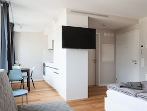 Une chambre d’hôtel moderne dotée d’une télévision à écran plat, d’une kitchenette, d’un coin repas et d’un espace nuit séparé.