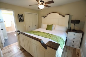 A bedroom with a bed, a nightstand, a ceiling fan, and a door.