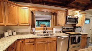 A kitchen with wooden cabinets, stainless steel appliances, a granite countertop, and a window with blinds.