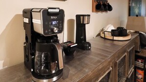 A coffee station with a Ninja espresso machine, a coffee grinder, and a coffee maker.