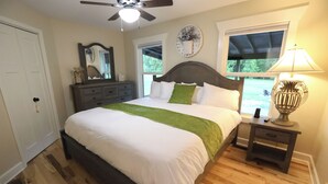 A bedroom with a bed, wooden flooring, a ceiling fan, a nightstand, and a window.