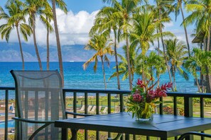 Un balcon avec vue sur l’océan, des palmiers et une chaise.