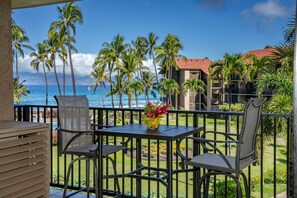 Ein Balkon mit Tisch und Stühlen, der Blick auf einen Strand mit Palmen und ein Gebäude im Hintergrund freigibt.