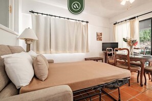 A hotel room with a bed, a desk, a chair, a TV, and curtains. - Amazing 1 BR Condo - Terrace - Pool - Romantic Zone (Puerto Vallarta)