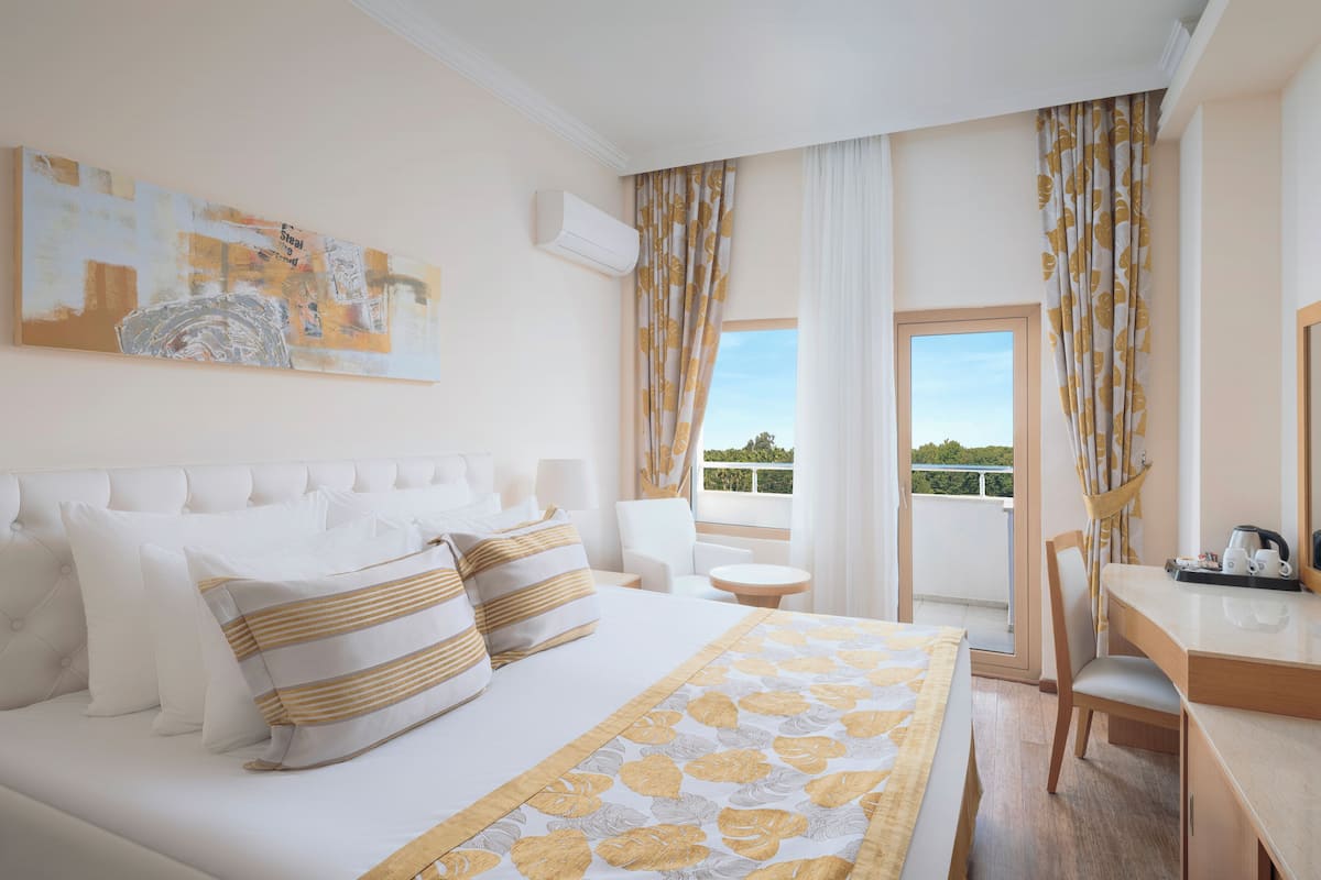 Habitación de hotel con cama, escritorio, silla y balcón con cortinas.
