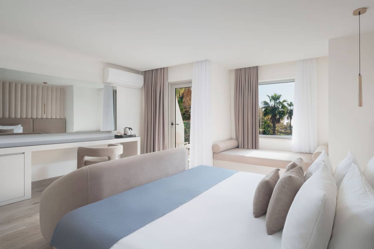 Una habitación de hotel moderna con una cama grande, un escritorio y una ventana con vista a palmeras.