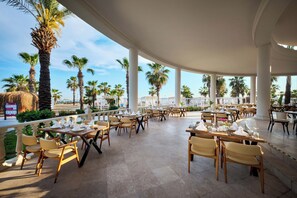 Un espace extérieur aménagé pour les repas, avec des tables et des chaises, des palmiers et une vue sur la ville.