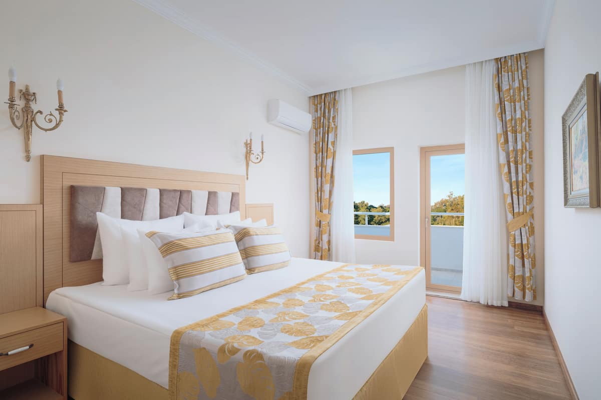 Un dormitorio con una cama grande, una mesita de noche, un aire acondicionado de pared y vistas al exterior a través de una ventana.
