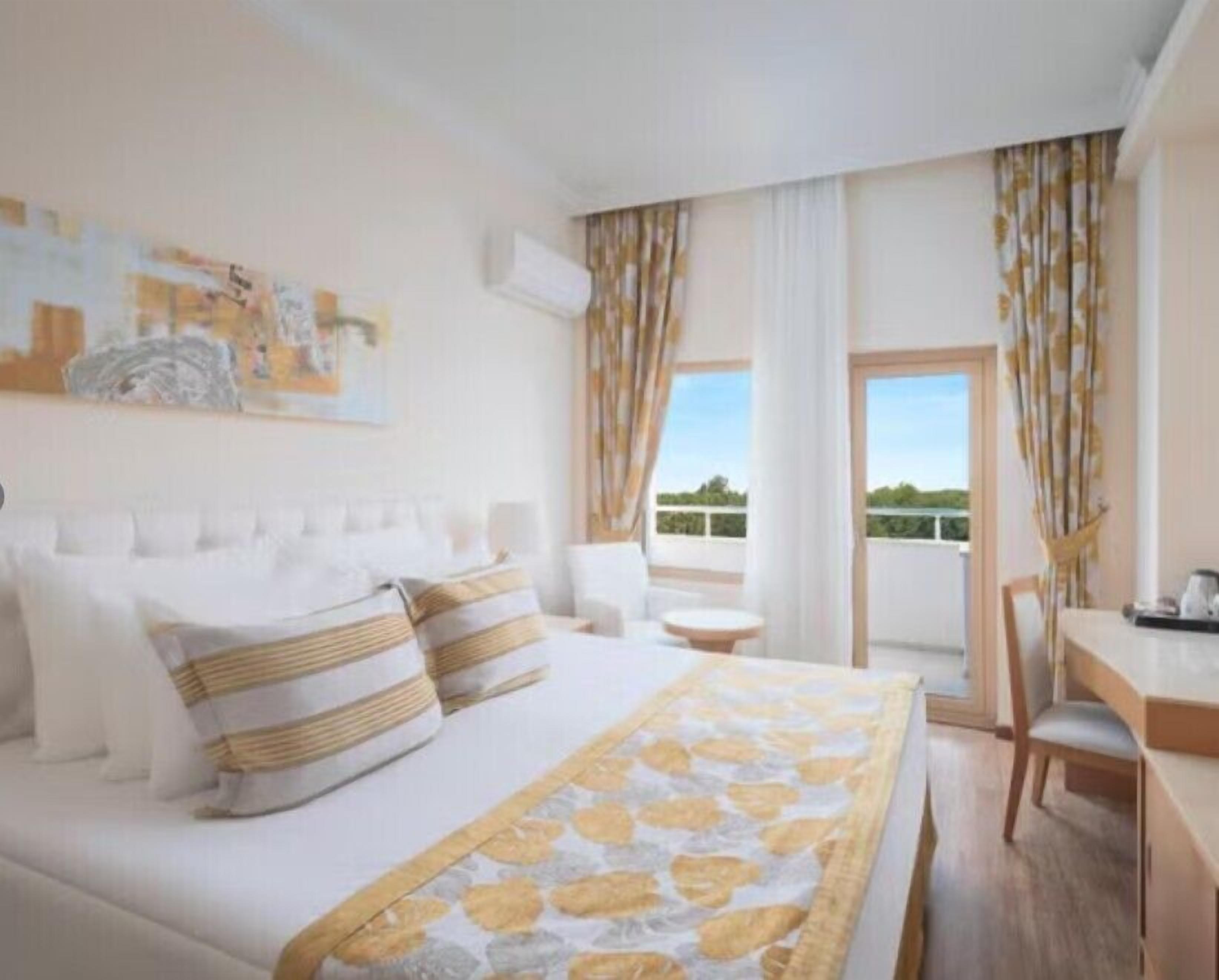 A hotel room with a bed, a small table, a chair, and a view of the outdoors.