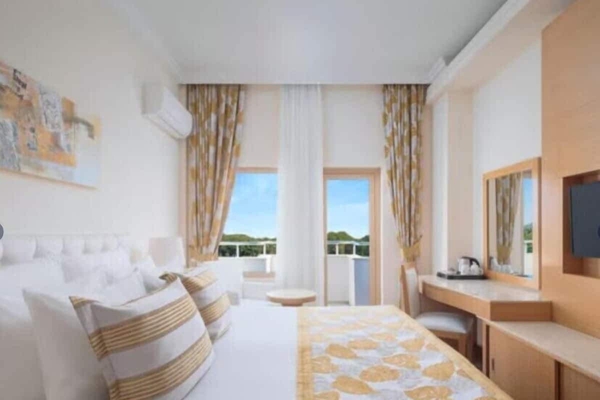 Habitación de hotel con cama, escritorio, silla, televisión y balcón con vistas.