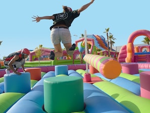 A person jumping over inflatable obstacles in an outdoor play area. - Magic Games (Oropesa del Mar)