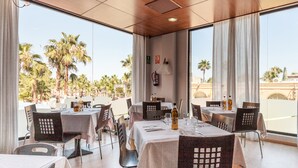 A restaurant with tables and chairs, large windows, and a view of palm trees. - Magic Games (Oropesa del Mar)